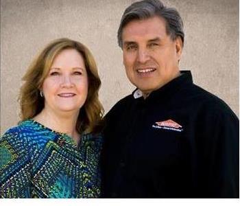 The owners smiling in front of a cream background.